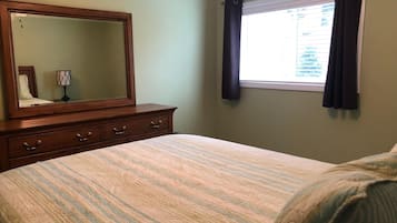 A bedroom with a large bed, a dresser with drawers, a mirror, and a window with curtains.