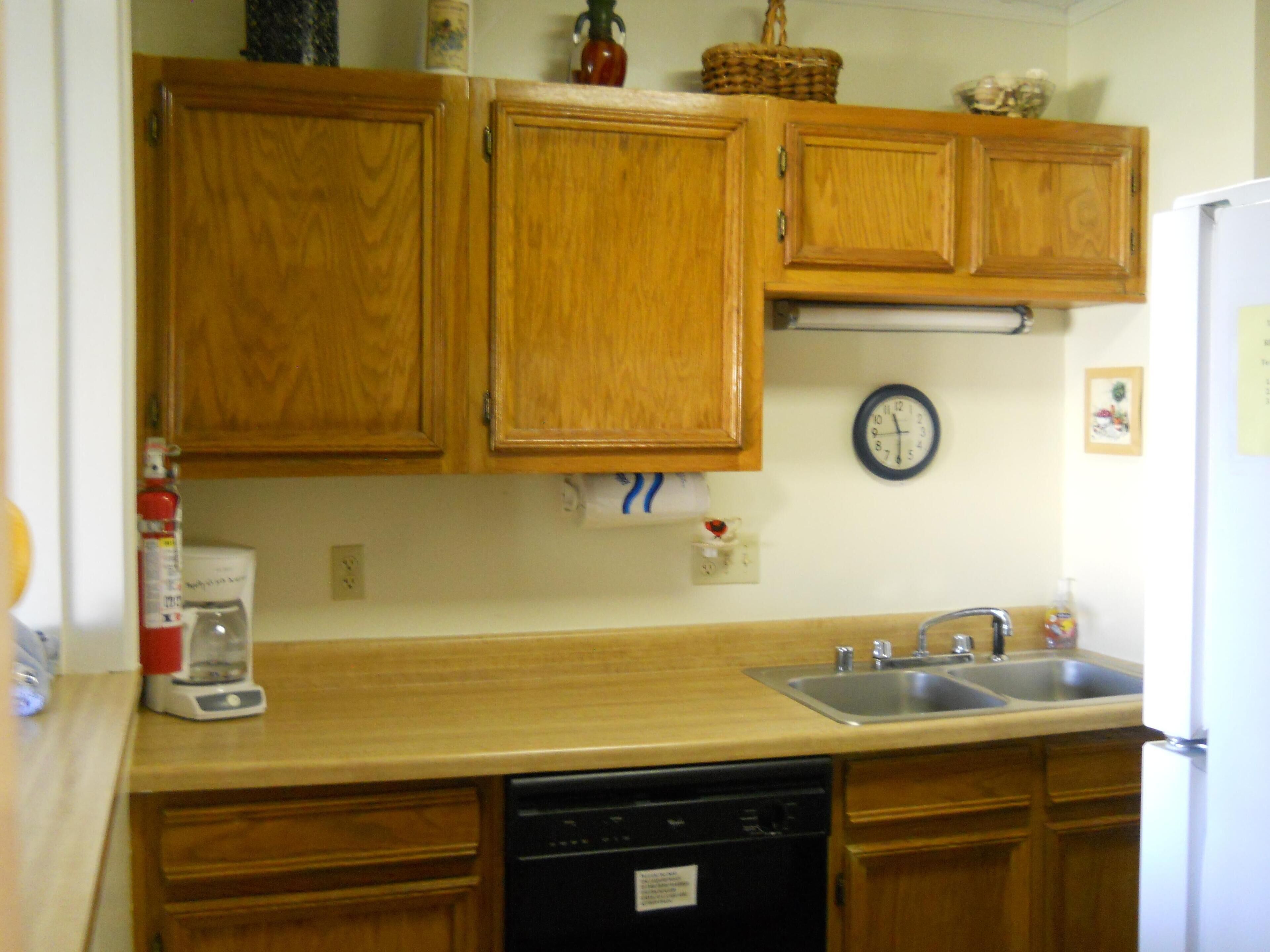 A kitchen with wooden cabinets, a sink, a dishwasher, and a clock on the wall.