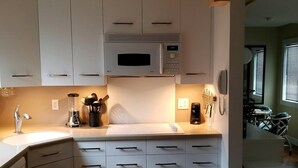 A modern kitchen with white cabinets, a microwave, a coffee maker, and a wooden cutting board on the counter. - Sugar Ski & Country Club Unit 11-403 Gold (Banner Elk)