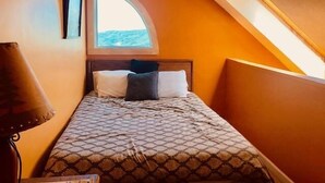 Ein kleines, gemütliches Schlafzimmer mit Bett, Fenster und Lampe.