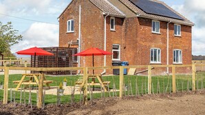 A two-story brick house with solar panels on the roof, a fenced garden area with wooden play structures, and a red umbrella. - Old Alton Hall Farmhouse (Holbrook, near Ipswich)