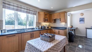A kitchen with wooden cabinets, a sink, and a table with a patterned tablecloth. - Old Alton Hall Farmhouse (Holbrook, near Ipswich)