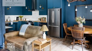 Een moderne keuken met een centraal eiland, een eetgedeelte met een houten tafel en stoelen, een bank en een hanglamp.
