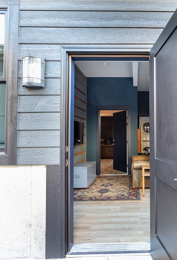 A doorway leading to a room with a patterned rug, a wooden bench, and a washing machine.