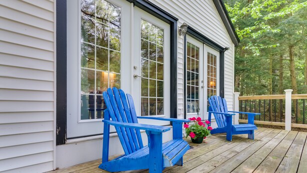 Una terraza de madera con dos sillas Adirondack azules y una maceta con flores rosas.