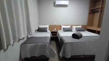 Une chambre d’hôtel avec deux lits, une armoire, un appareil de climatisation et une table de chevet avec un téléphone.