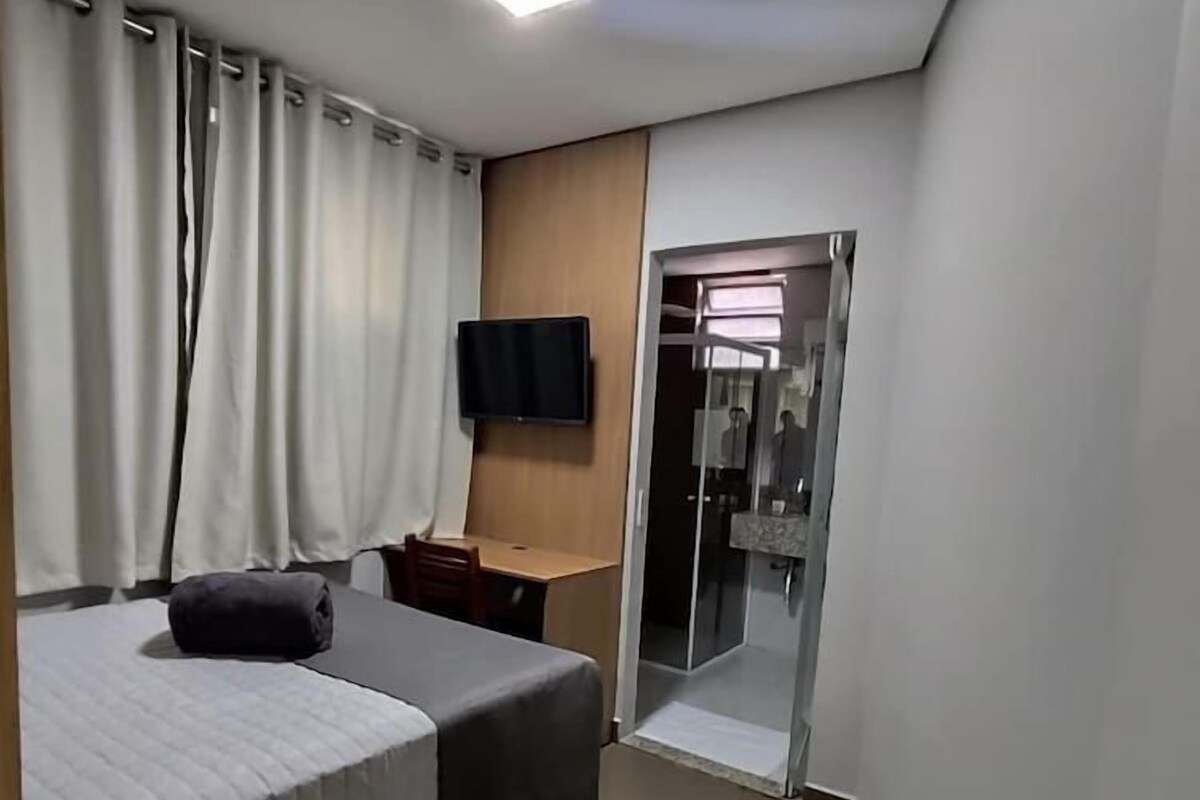 Une chambre d’hôtel équipée d’un lit, d’un bureau, d’une chaise, d’une télévision et d’une porte coulissante donnant accès à la salle de bain.