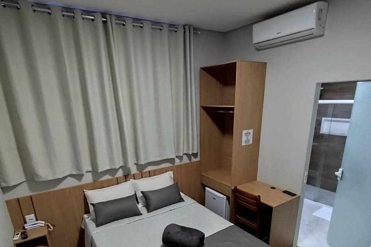 Habitación de hotel con cama, escritorio, silla, armario y equipo de aire acondicionado.