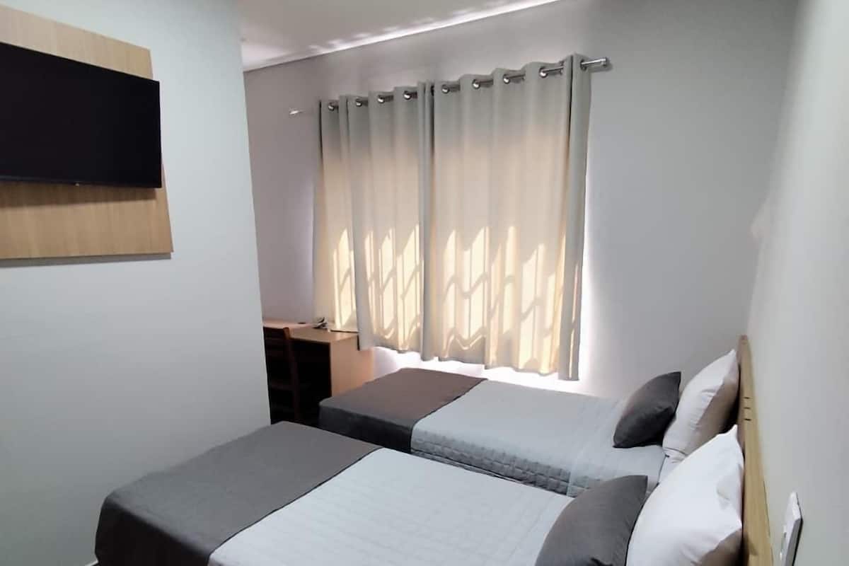 Habitación de hotel con dos camas, un escritorio y una ventana con cortinas.