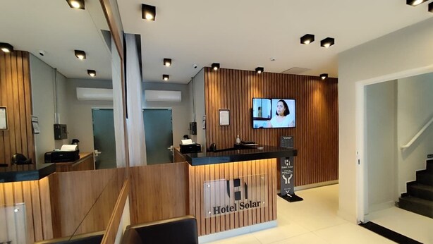 Ein Hotel-Rezeptionsbereich mit einem hölzernen Empfangstresen, einem Flachbildfernseher und einer Treppe rechts.