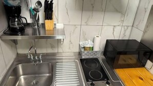 A compact kitchen with a stainless steel sink, a built-in stove, and a microwave. There is a wooden shelf with kitchen utensils and a coffee maker. - 14 on the Ridge, Pet Friendly! (Pigeon Forge)