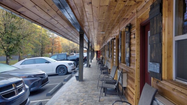 A covered outdoor seating area with wooden beams and stone flooring, adjacent to a building with large windows and a red door. - 14 on the Ridge, Pet Friendly! (Pigeon Forge)