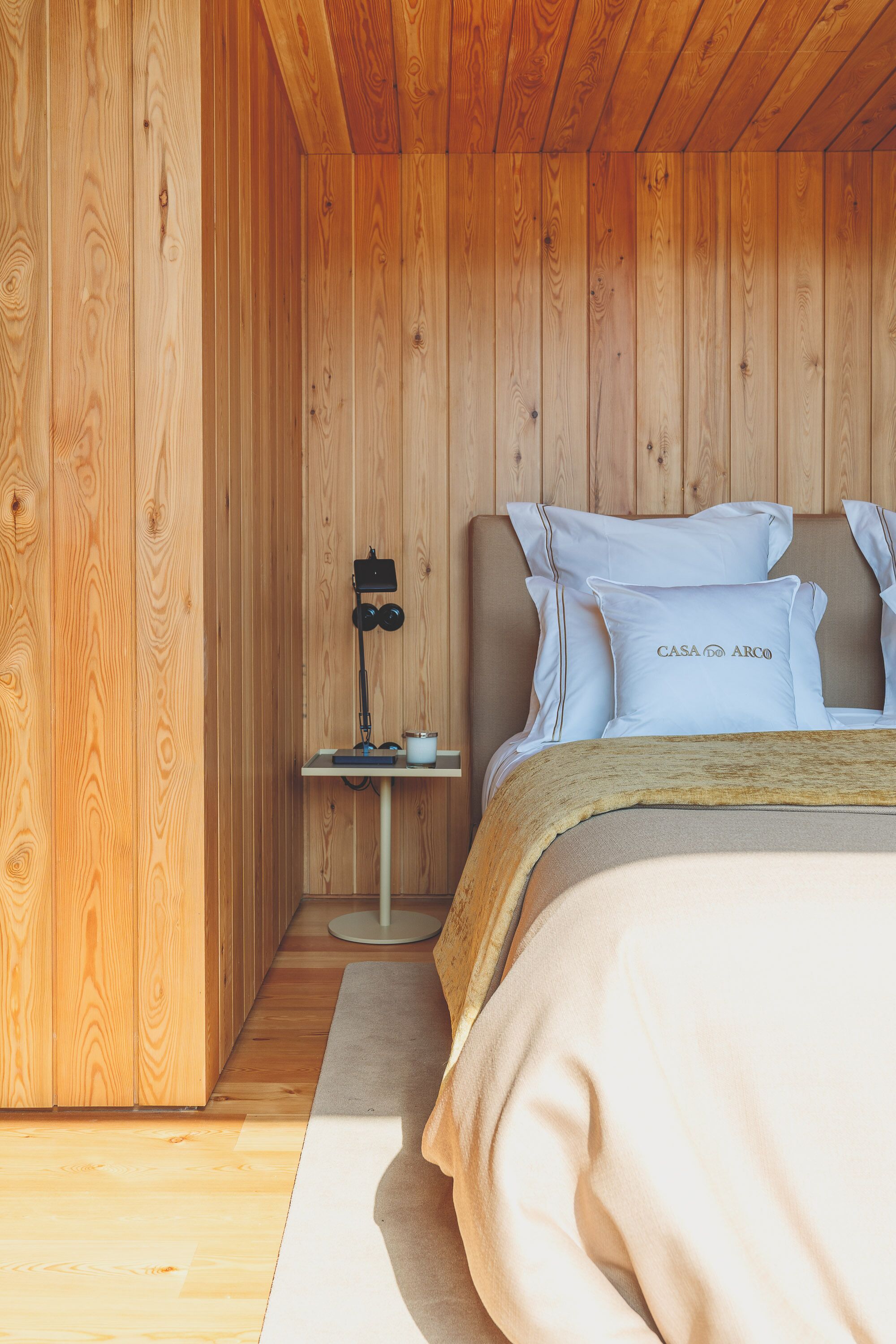 A wooden-paneled room with a bed, pillows, a bedside table, and a lamp.
