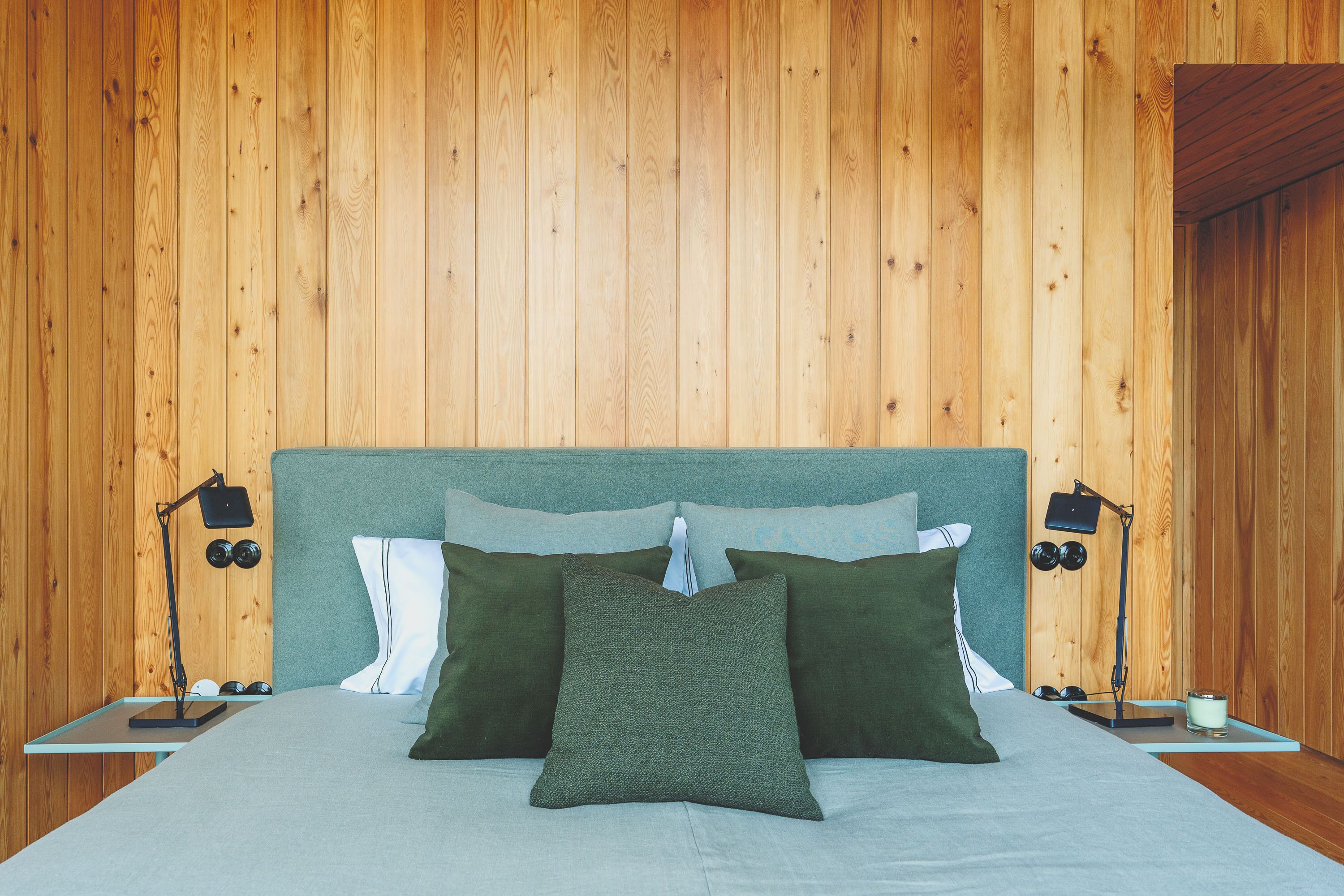 Un dormitorio con paneles de madera, una cama, almohadas y lámparas de noche.