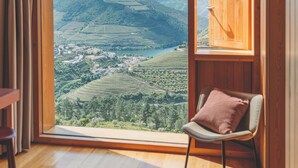 Una habitación con un amplio ventanal que ofrece vistas a un paisaje montañoso y una pequeña silla con cojín.