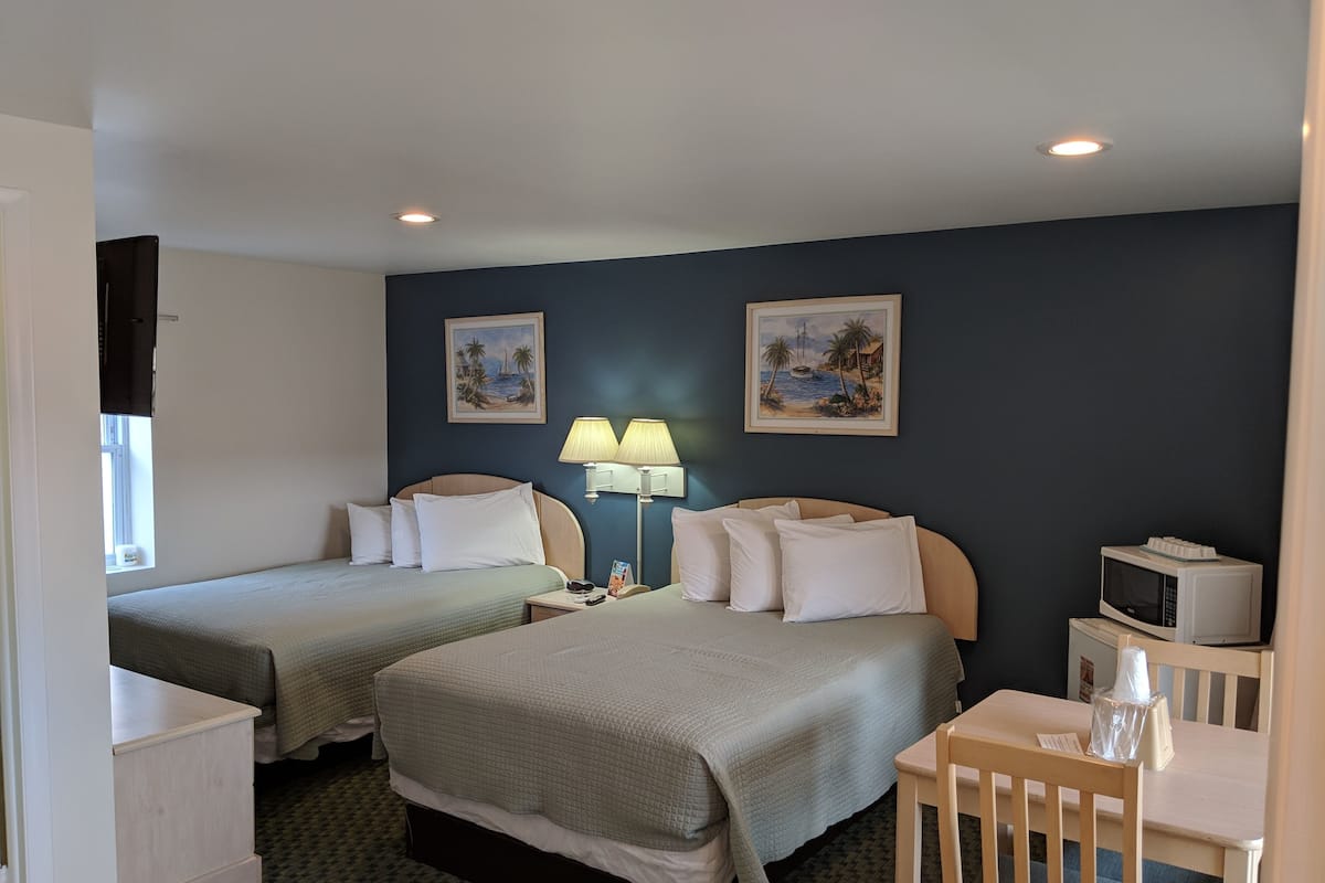A hotel room with two single beds, a desk with a chair, a microwave, and two wall-mounted lamps.