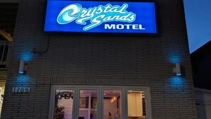 A motel sign with the name "Crystal Sands Motel" and a window displaying interior lighting and a chair. - Crystal Sands Motel (Ocean City)