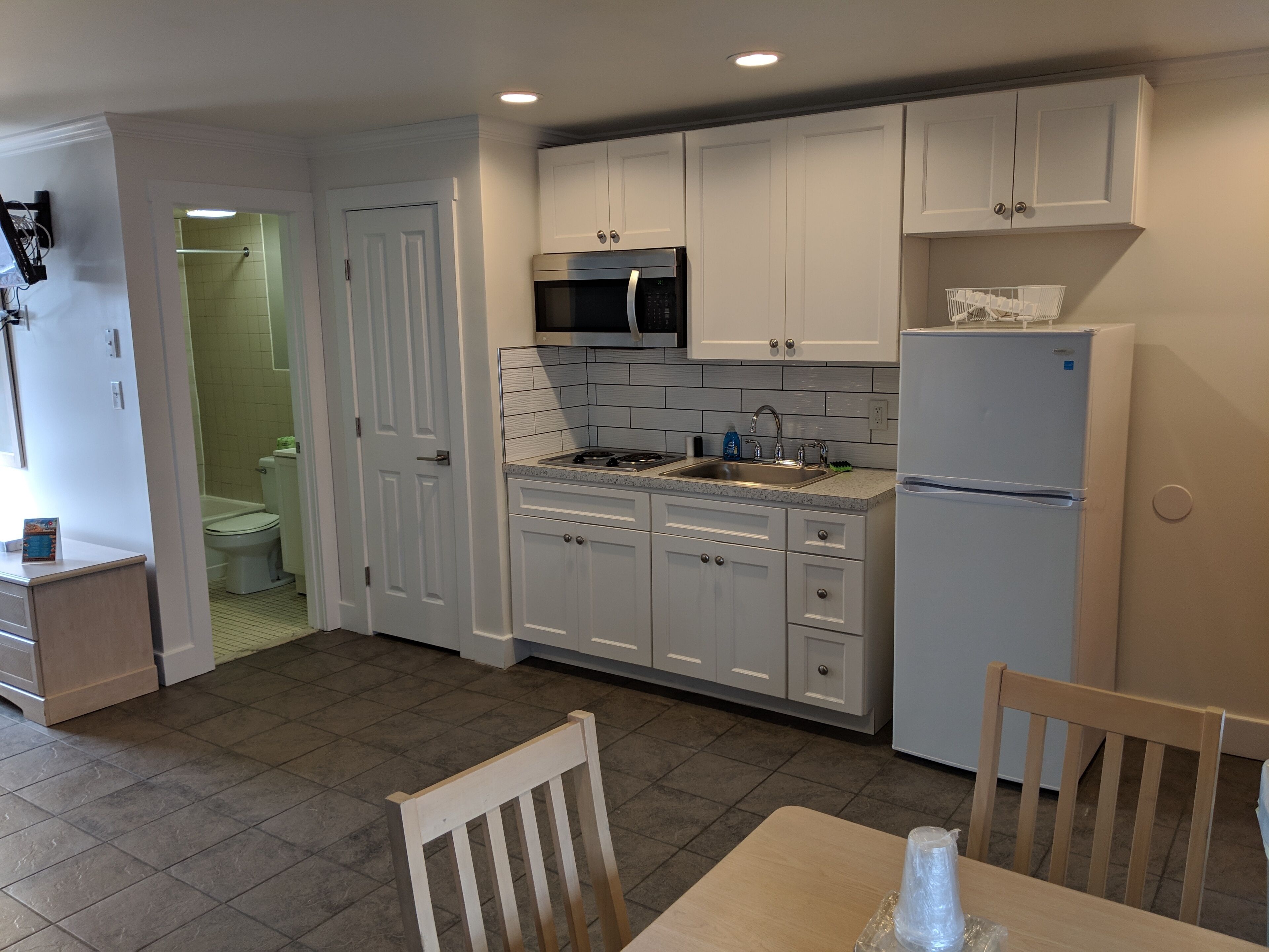 A modern kitchen with white cabinets, a stainless steel refrigerator, and a microwave.