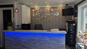 A reception desk with a stone-textured counter, a 'Coca-Cola' sign, a flat-screen TV, and a fruit display. - Crystal Sands Motel (Ocean City)