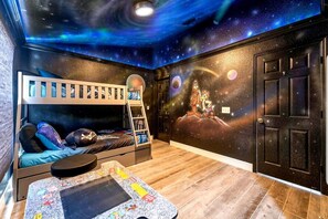 Cozy space for kids, featuring a bunk bed with ladder, desk, and a fun space-themed mural.