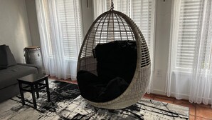 Ein Wohnzimmer mit Hängekorbsessel, Sofa, kleinem Tisch und einem gemusterten Teppich.