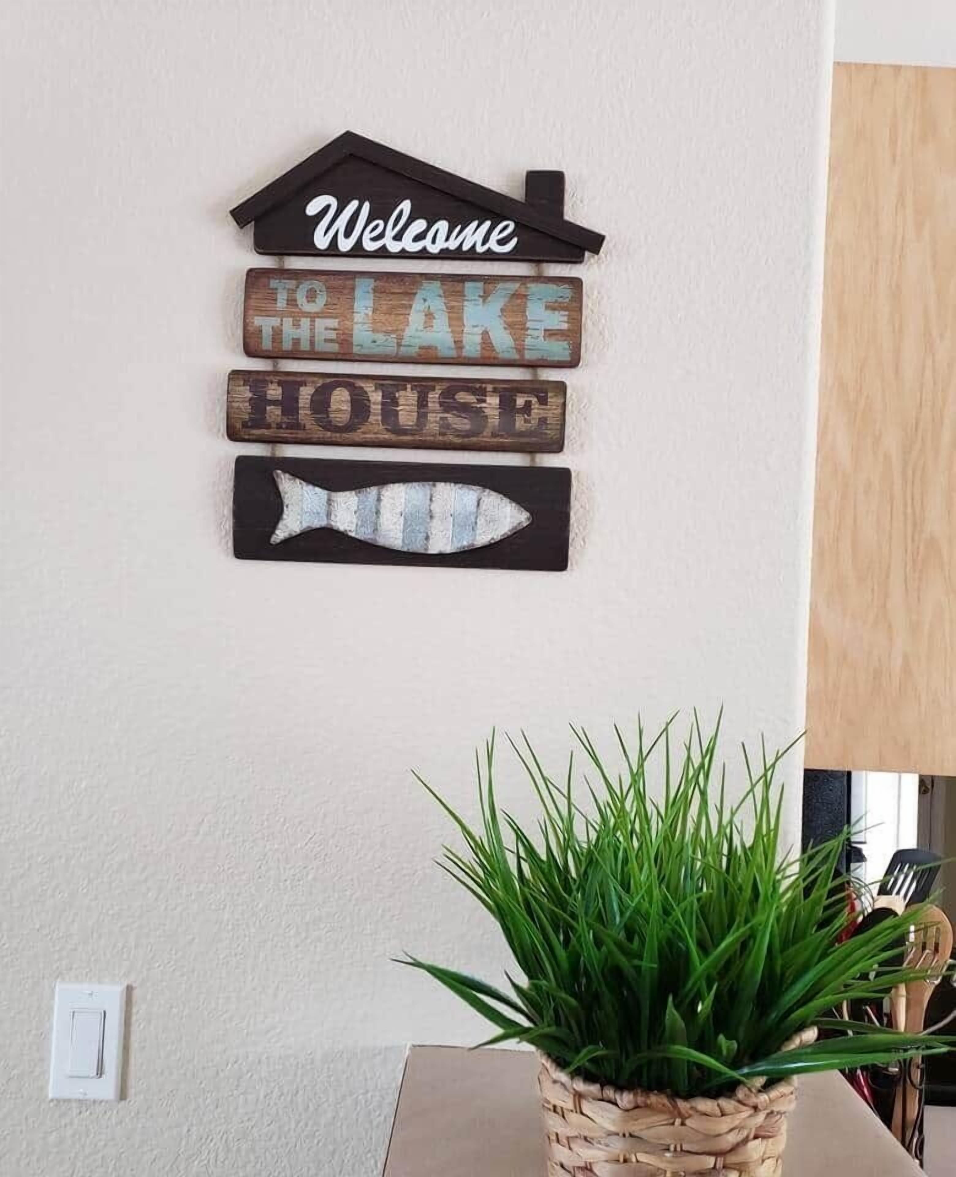 Un letrero montado en la pared con la frase 'Welcome to the Lake House' y una decoración de pescado.