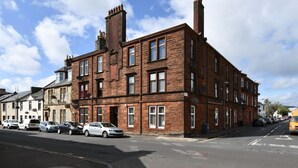 A multi-story brick building with a row of parked cars along the street.