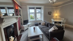 A living room with a fireplace, a sofa, a coffee table, a TV, and a dining area with a table and chairs.