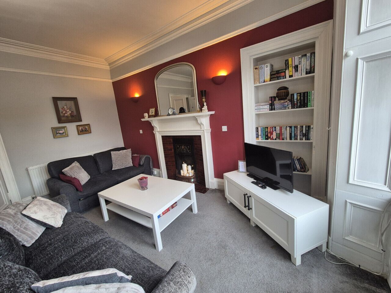 A living room with a fireplace, a sofa, a coffee table, a TV stand, and a bookshelf.