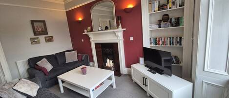 A living room with a fireplace, a sofa, a coffee table, a TV stand, and a bookshelf.