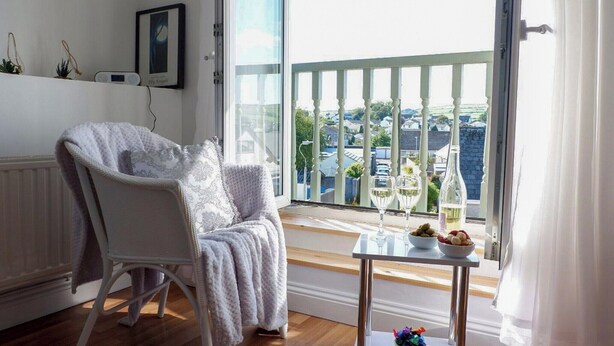 A cozy room with a white chair, a small table with a bowl of fruit, and a view of a balcony with a railing. - 2 bedroom accommodation in Swarthmoor, near Ulverston (Swarthmoor, near Ulverston)
