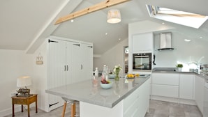 A modern kitchen with white cabinetry, a granite countertop, and a built-in oven. - Charming Cottage, Wi-Fi, Parking, Pets Accepted (Newquay)
