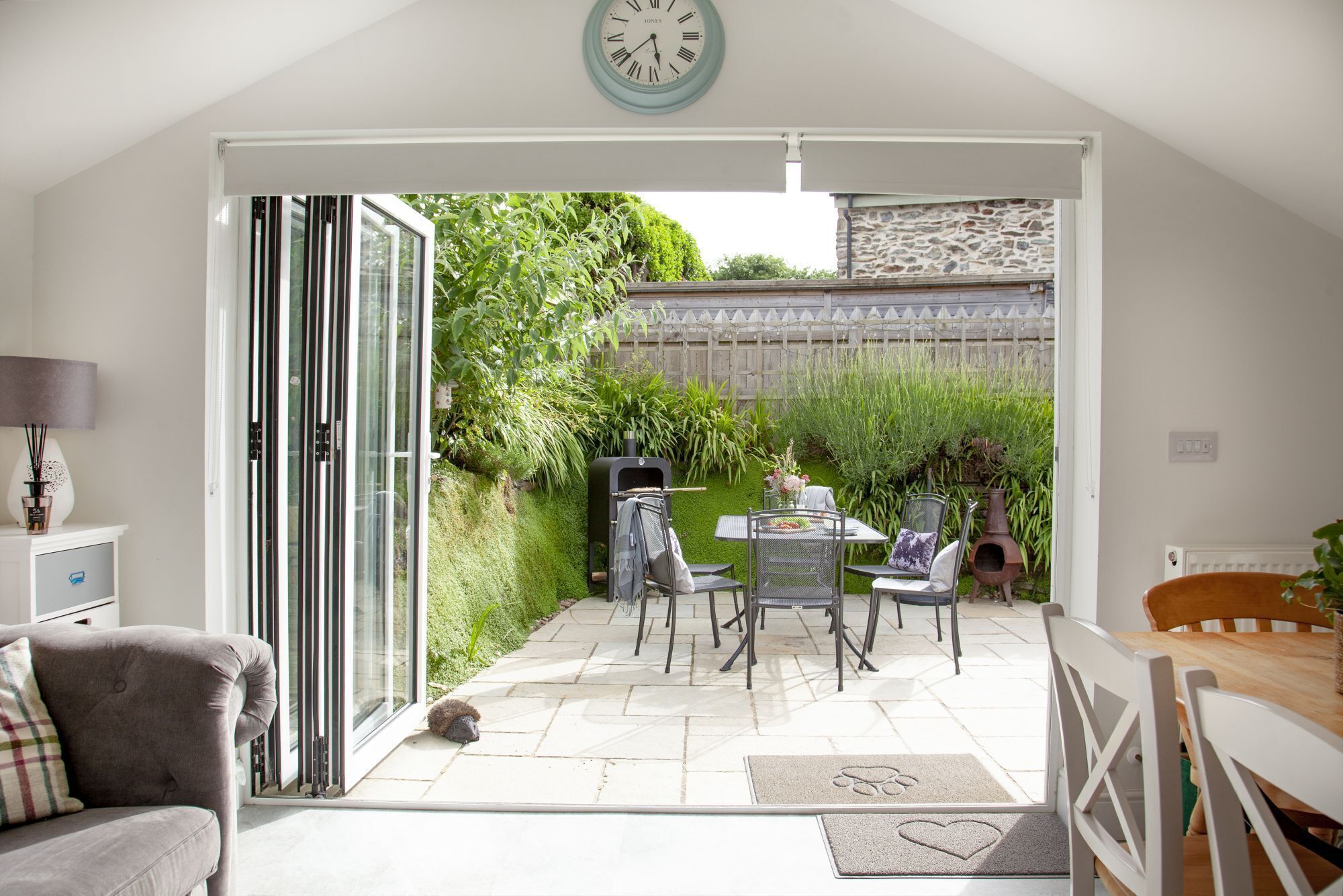 Un patio moderno con una porta vetrata che si apre su un giardino, mobili da esterno e un muro in pietra.