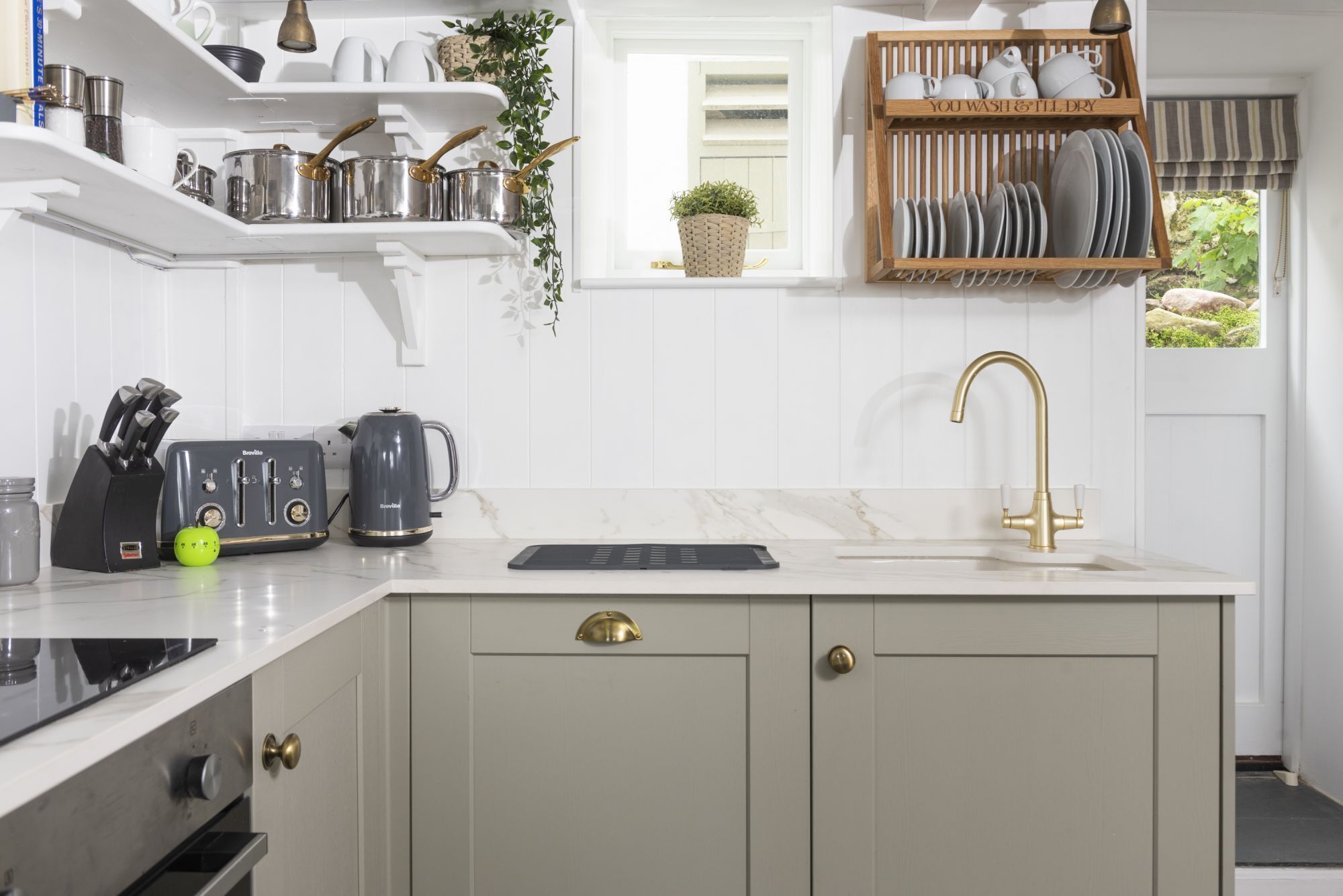 A kitchen with white cabinets, a black countertop, a gold faucet, and a window with a view of greenery.