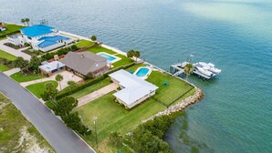 Ein Luftbild einer Küstenimmobilie mit Swimmingpool, einer Anlegestelle für Boote und einem gepflegten Rasen.