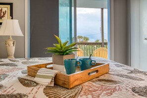 Een houten dienblad met een plant, een gestreept kleedje en drie blauwe mokken op een bed met een bedovertrek met dessin.
