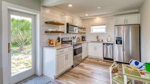 A modern kitchen with white cabinetry, stainless steel appliances, and a small dining area with a table and chairs. - Barefoot Hideaway (St. Augustine)