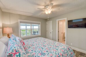 A bedroom with a bed, a ceiling fan, a window with a view, and a door leading to another room. - Barefoot Hideaway (St. Augustine)