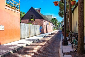 A narrow cobblestone street lined with buildings, including a hospital and a building with a sign reading "Hospital Militar." - Villas at Ocean Gate (St. Augustine)