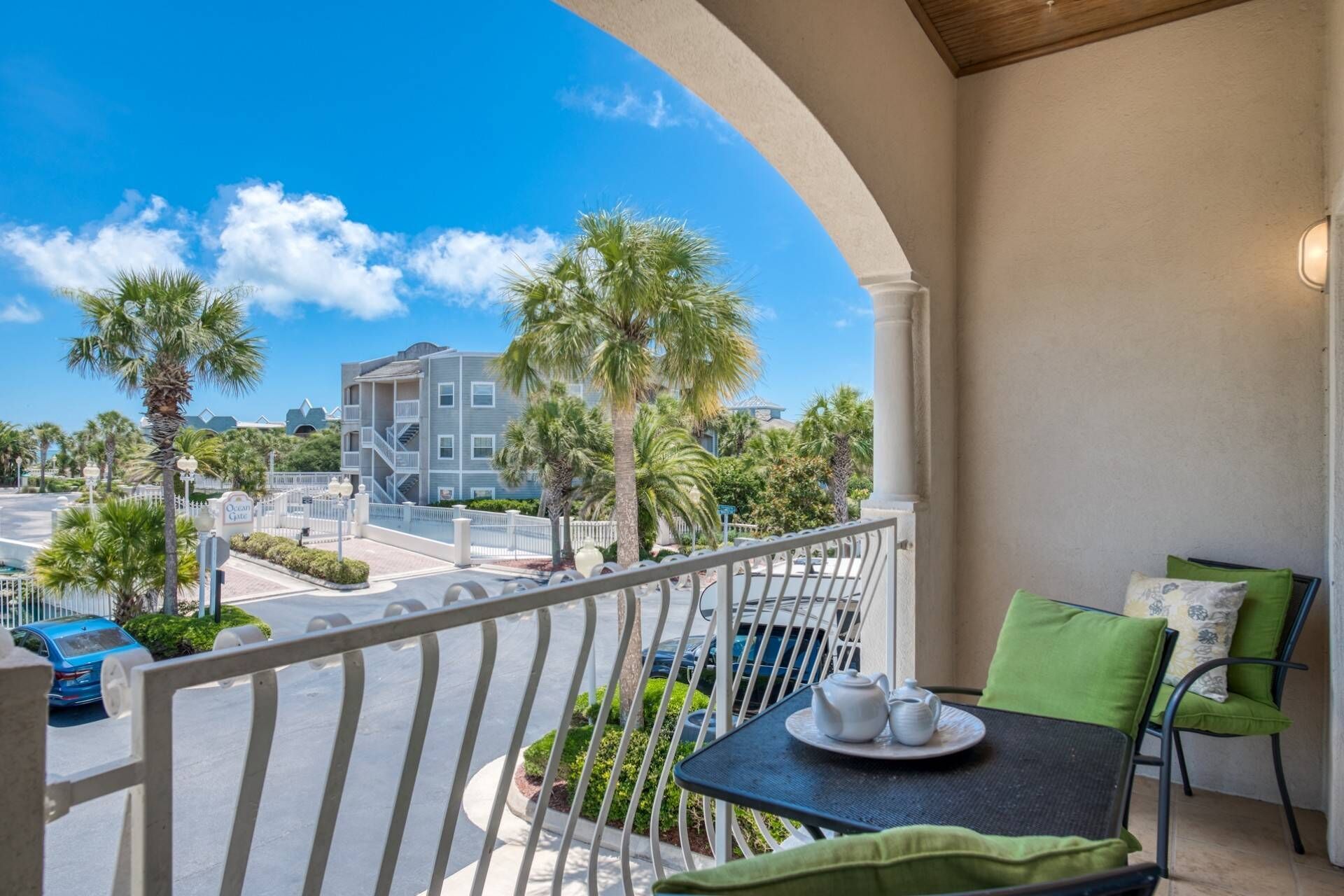 A balcony with a table set for tea, overlooking a street with palm trees and a building.