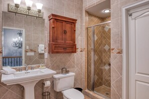A bathroom with a sink, toilet, and shower. There is a wooden cabinet above the sink and a mirror with a chandelier. - Villas at Ocean Gate (St. Augustine)