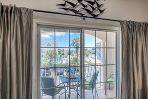 A room with a large sliding glass door leading to an outdoor patio. The patio has a table and chairs, and the view includes a building and palm trees. - Villas at Ocean Gate (St. Augustine)