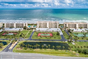 A coastal hotel complex with multiple buildings, a tennis court, and a body of water.