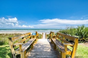 A wooden boardwalk leading to a beach with benches and a sign warning about sea turtles.