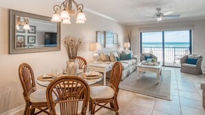 A spacious living area with a dining table, chairs, a sofa, and a balcony with a view of the ocean. - Crescent Beach Condos (St. Augustine)