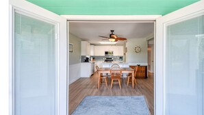 A modern kitchen with white cabinets, a wooden dining table, and a ceiling fan.