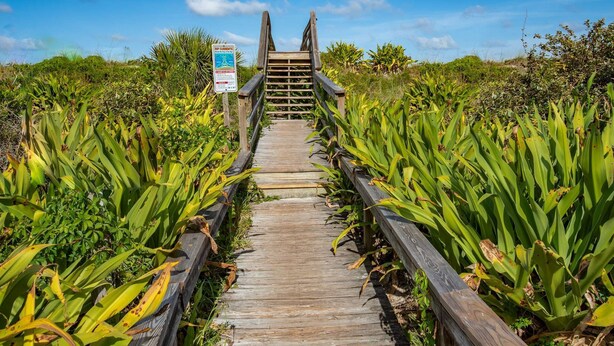 A wooden boardwalk leading to a wooden structure with a sign warning of rip currents.