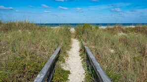 A sandy path flanked by wooden railings leading to a beach.