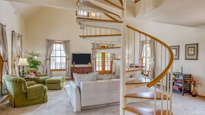 Ein geräumiges Wohnzimmer mit einer Wendeltreppe, einem großen Bett, grünen Sesseln und einem Fernseher.
