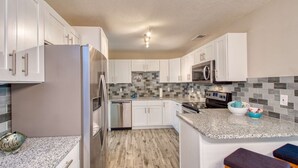 A modern kitchen with white cabinets, a stainless steel refrigerator, a microwave, and a granite countertop. - 28 Solano (St. Augustine)